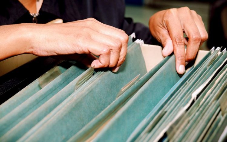 Person looking through a filing cabinet full of green files.